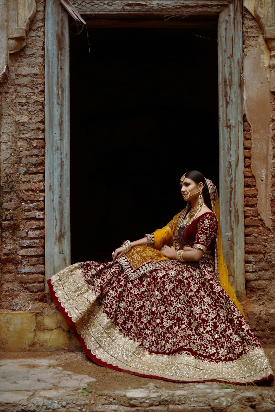 Woman in a maroon velvet lehenga sitting in a doorway